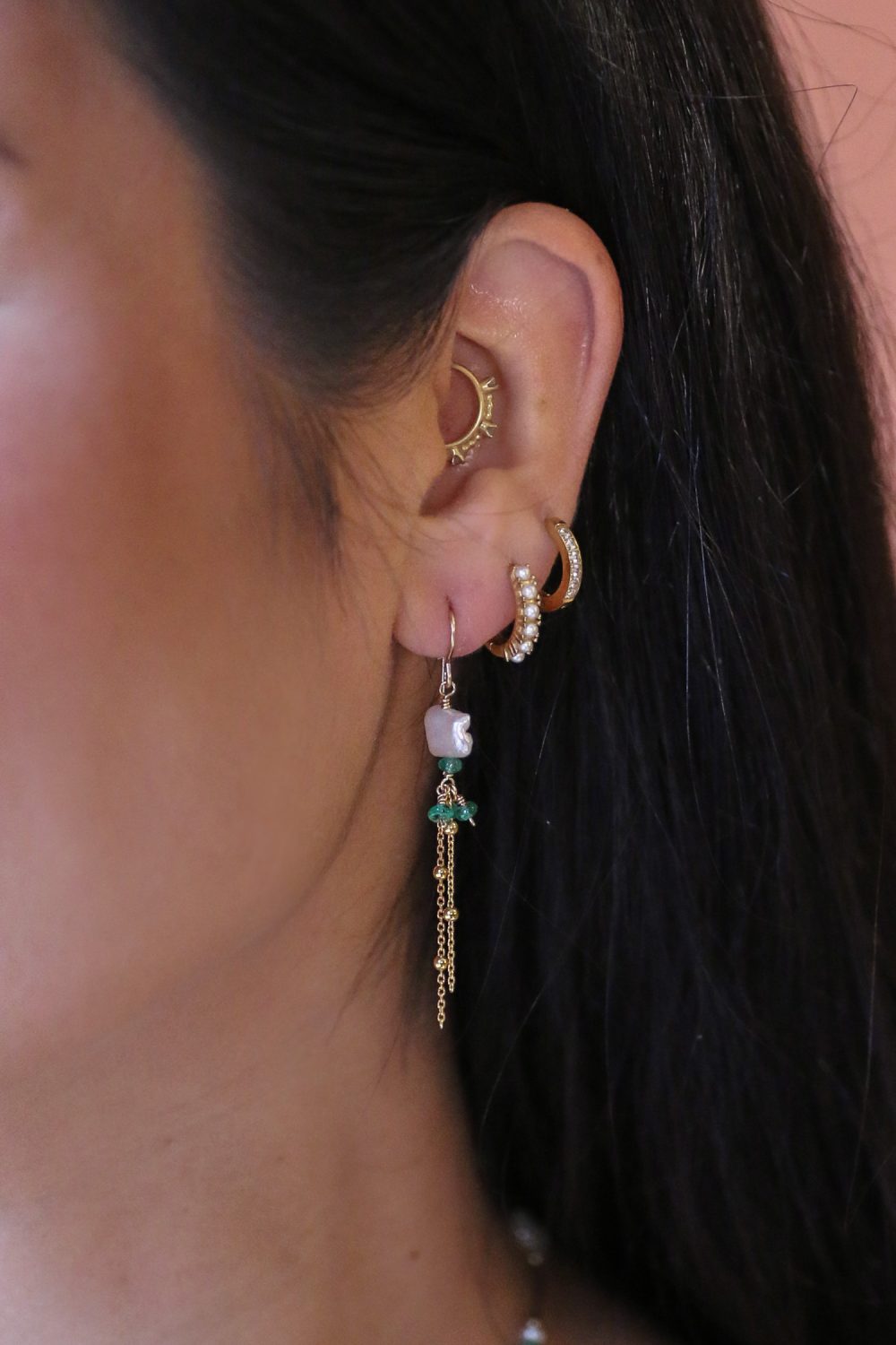 het model draagt lange gouden oorbellen met een witte biwa zoetwaterparel en grasgroene kleine smaragd edelstenen