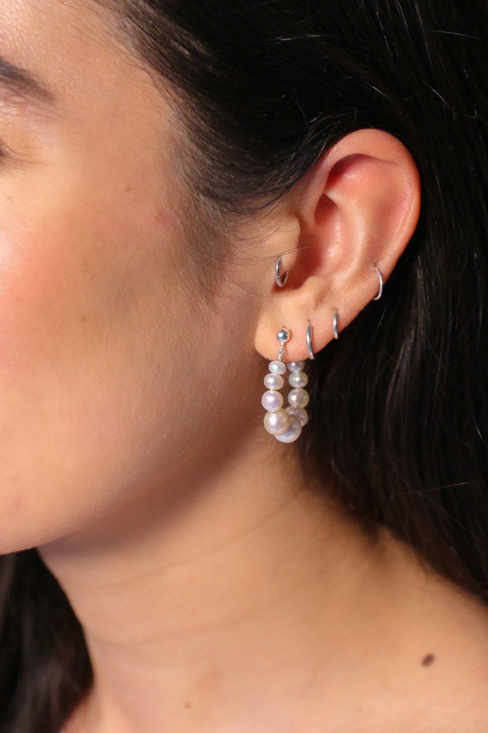 het model draagt oorringen van witte glanzende zoetwaterparels in maat oplopend naar het midden. De oorringen sluiten met een zilveren oorsteker door het oor.