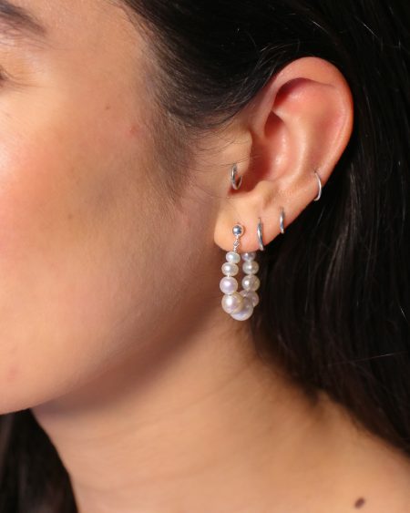 het model draagt oorringen van witte glanzende zoetwaterparels in maat oplopend naar het midden. De oorringen sluiten met een zilveren oorsteker door het oor.