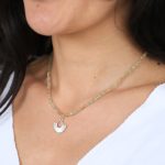 het model draagt een edelsteen ketting van zonnesteen en groene peridoot. Aan de ketting hangt een grote zilveren hanger in de vorm van zonnestralen