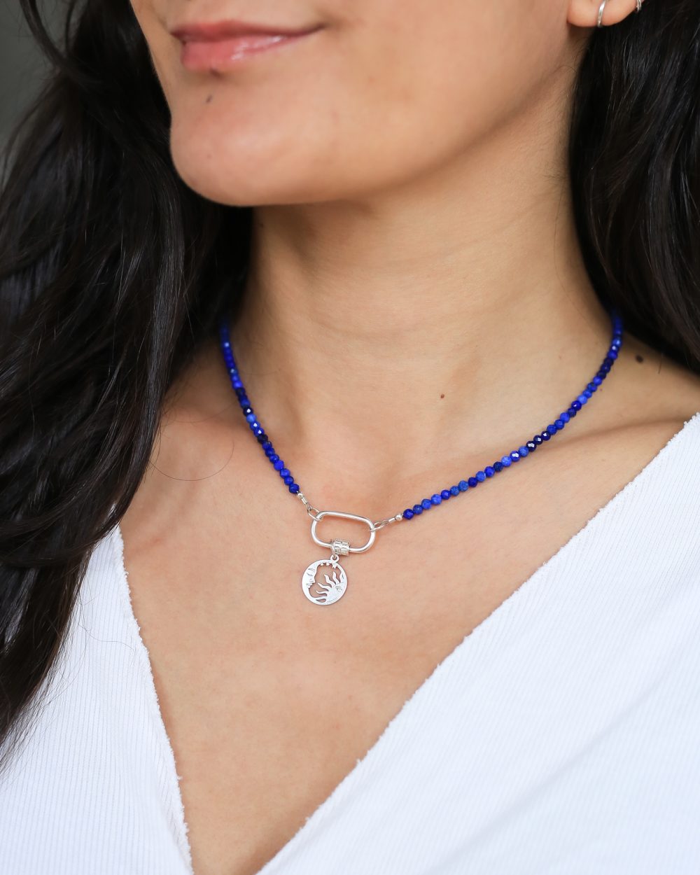 om de hals een diepblauwe lapis lazuli edelsteen ketting met aan de voorkant een grote zilveren schroefsluiting en een zilveren zon-en maan hanger