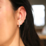 het model draagt een geheel zilveren oorring van gevlochten zilver.