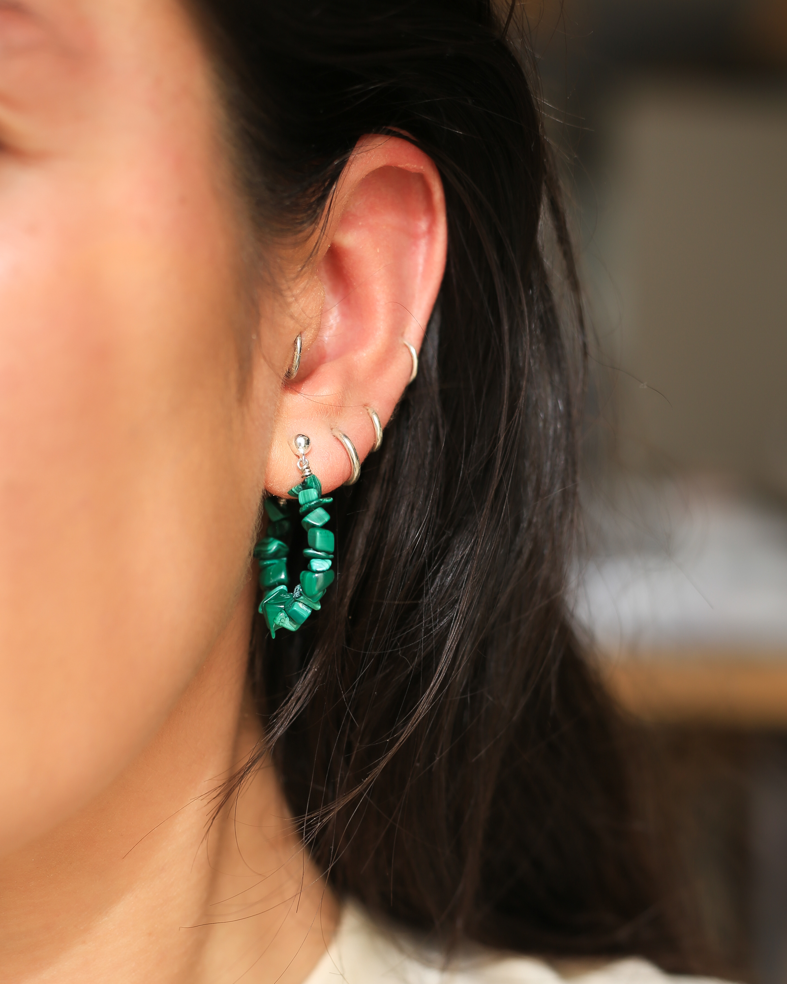 Het model draagt oorringen met groene Malachiet edelsteen brokjes . De oorringen sluiten met een zilveren steker door het oor.