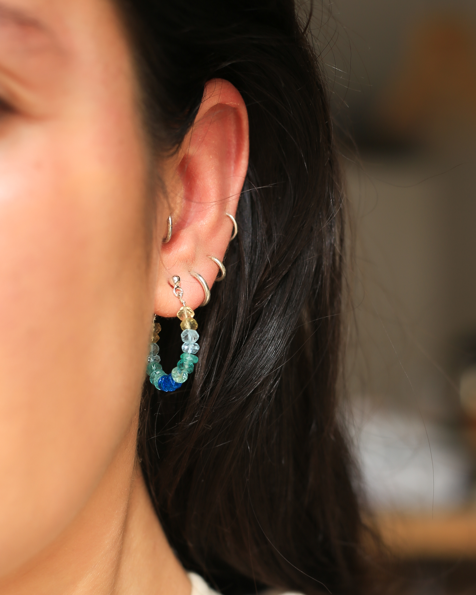 het model draagt oorringen van de edelstenen blauwe apatiet, lichtblauwe aquamarijn en gele citrien. De oorringen hebben zilveren stekers door het oor.