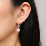 model draagt een korte zoetwater pareloorbel van een witte parel, met verguld Thais zilver en geoxideerd zilver uit Bali