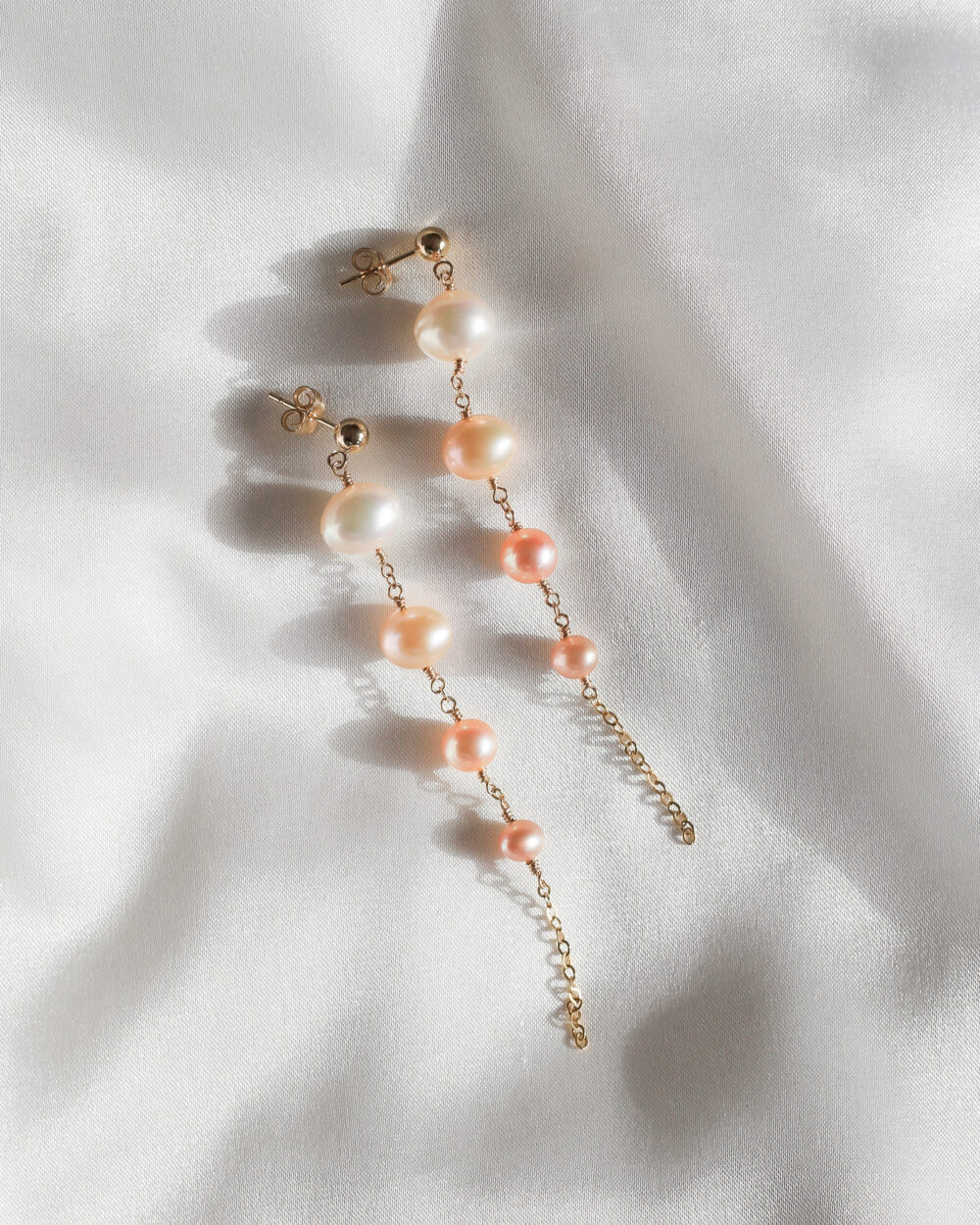 Swayng Pearls lange glanzende parel oorhangers met vier zoetwaterparels in kleur van wit naar donkerzalm tussen een gouden ketting verwerkt.