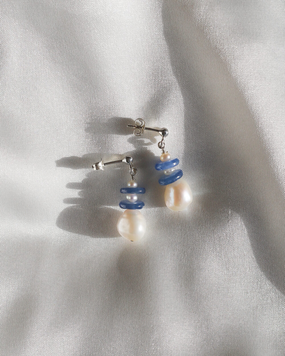 korte zilveren oorhanger met grote glanzende zoetwaterparel en blauwe kyaniet schijfjes en kleine parels.